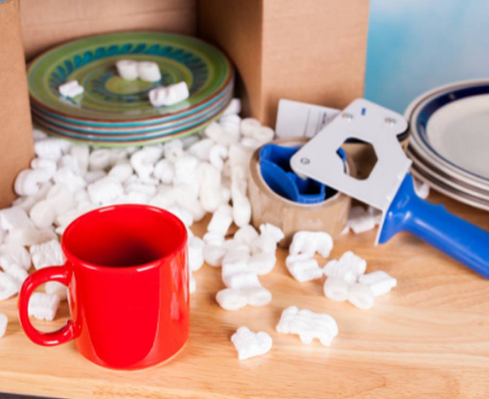 Kubek i talerze przygotowane do spakowania, skropak i dyspenser do taśmy pakowej